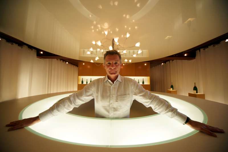 Didier Depond - Salon. Didier stands in the new tasting room at Salon. The lit table like the base of a marie antoinette champagne glass, he becomes the stem, the ceiling the wide bowl and the lights with their reflections, the bubbles rising.